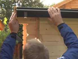 Gartenhaus Dachrinne montieren - Mann hängt Dachrinne ein