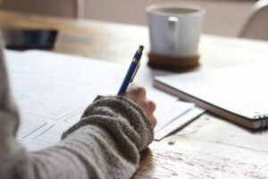 Sauna Planung - Person schreibt auf Papier am Schreibtisch mit Kaffeetasse