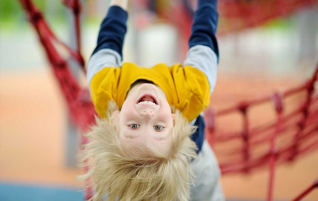 Fallschutz Spielplatz - Kind kopfüber an Kletterturm