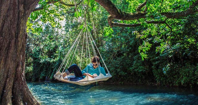 Tiipii Hängezelt über den Fluss an einem Baumstamm hängen, ein Mensch liest ein Buch 